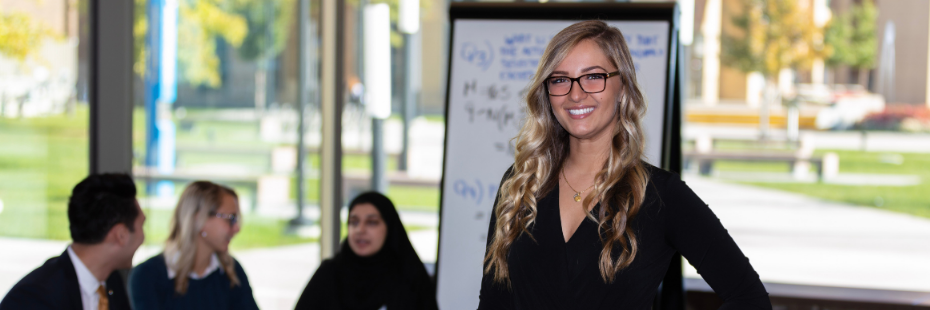 Business student smiling at the camera with three other students talking in the background