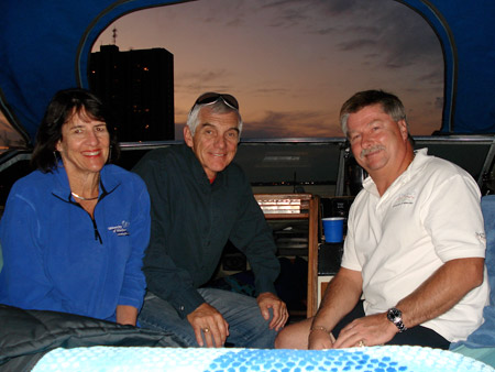 Dorothy Spiller, Alan Wright and Rick Kiza sit in a boat.  Sun setting in background.