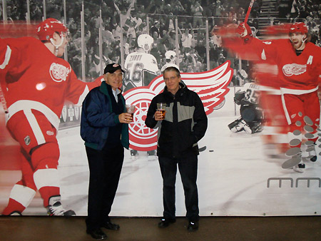 Alan and Gordon pose in front of a giant poster featuring players from of the famous Red Wings hockey club.