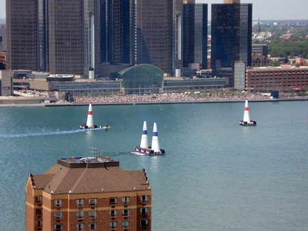 A plane is about to fly through two inflated pylons on the Detroit River. The Renaissance Center is in the background.