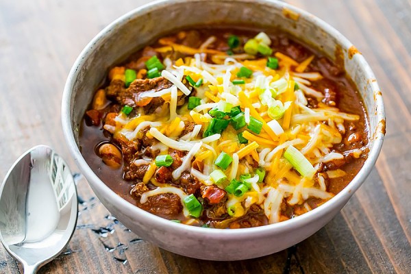bowl of chili topped with green onion, sour cream, cheddar cheese