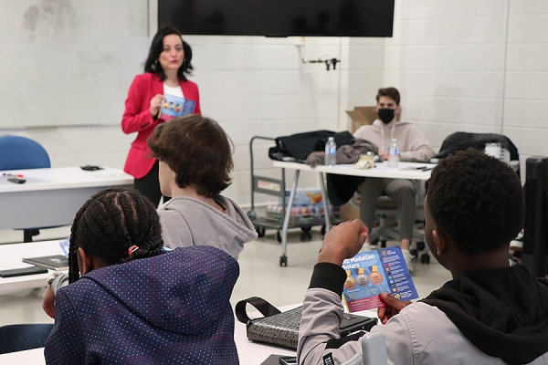 Professor stands at front of classroom with high school students taking notes