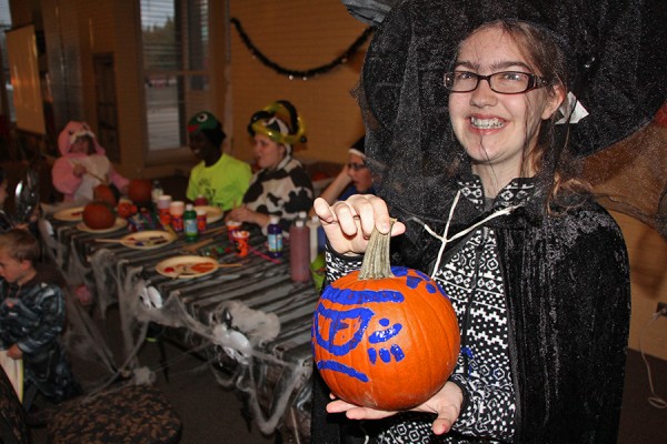 Kid dressed as witch displaying painted pumpkin