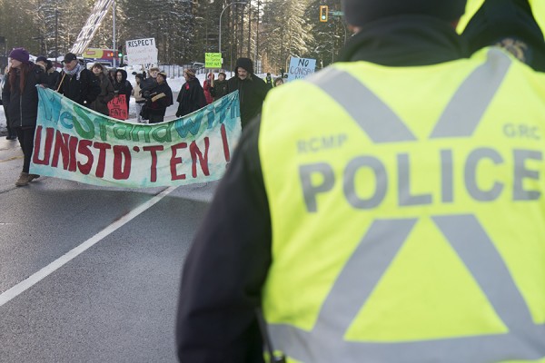 Man in RCMP vest watching protest marchers