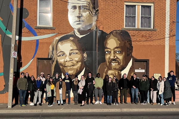 students standing below mural of historical Black figures