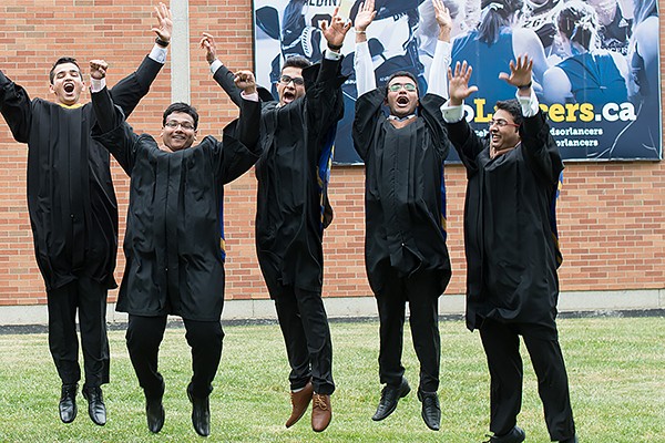 Graduands wearing academic robes jump in the air