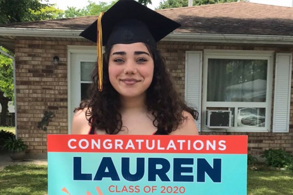 Young woman wearing mortarboard and holding sign that reads &quot;Congraulations Lauren&quot;