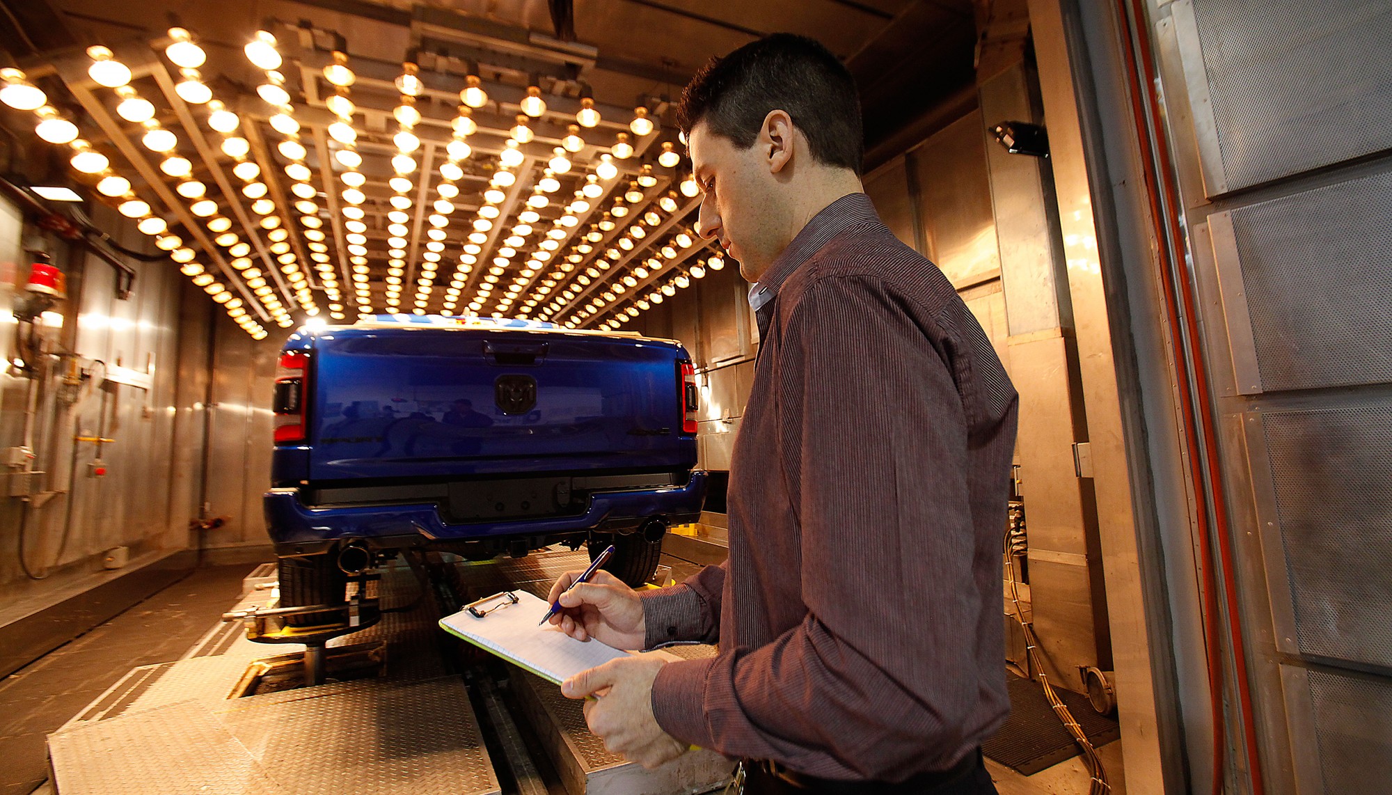 A student examines a vehicle under heat testing lamps.