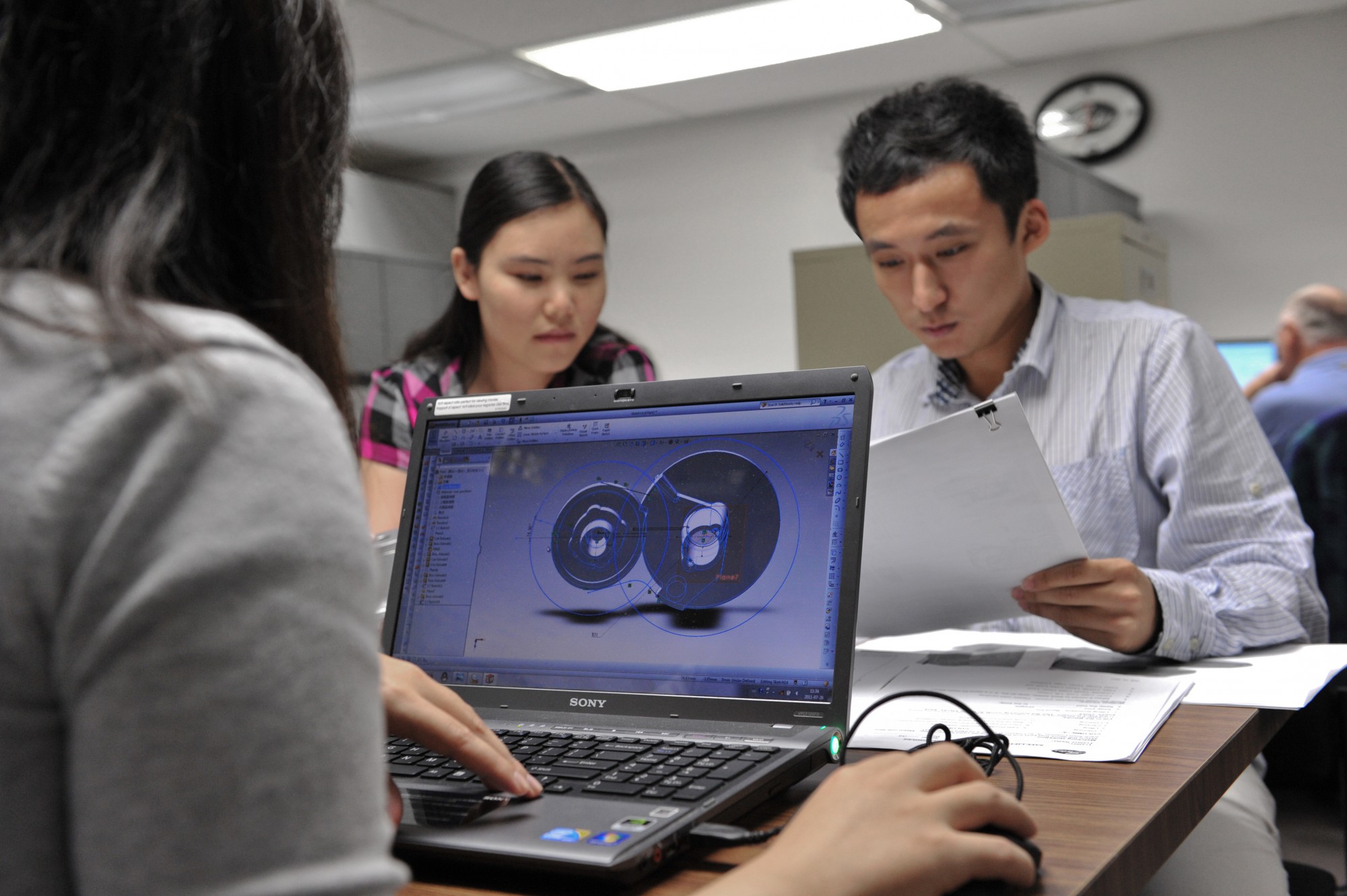 Two engineering students discussing written content while one student Laptop.