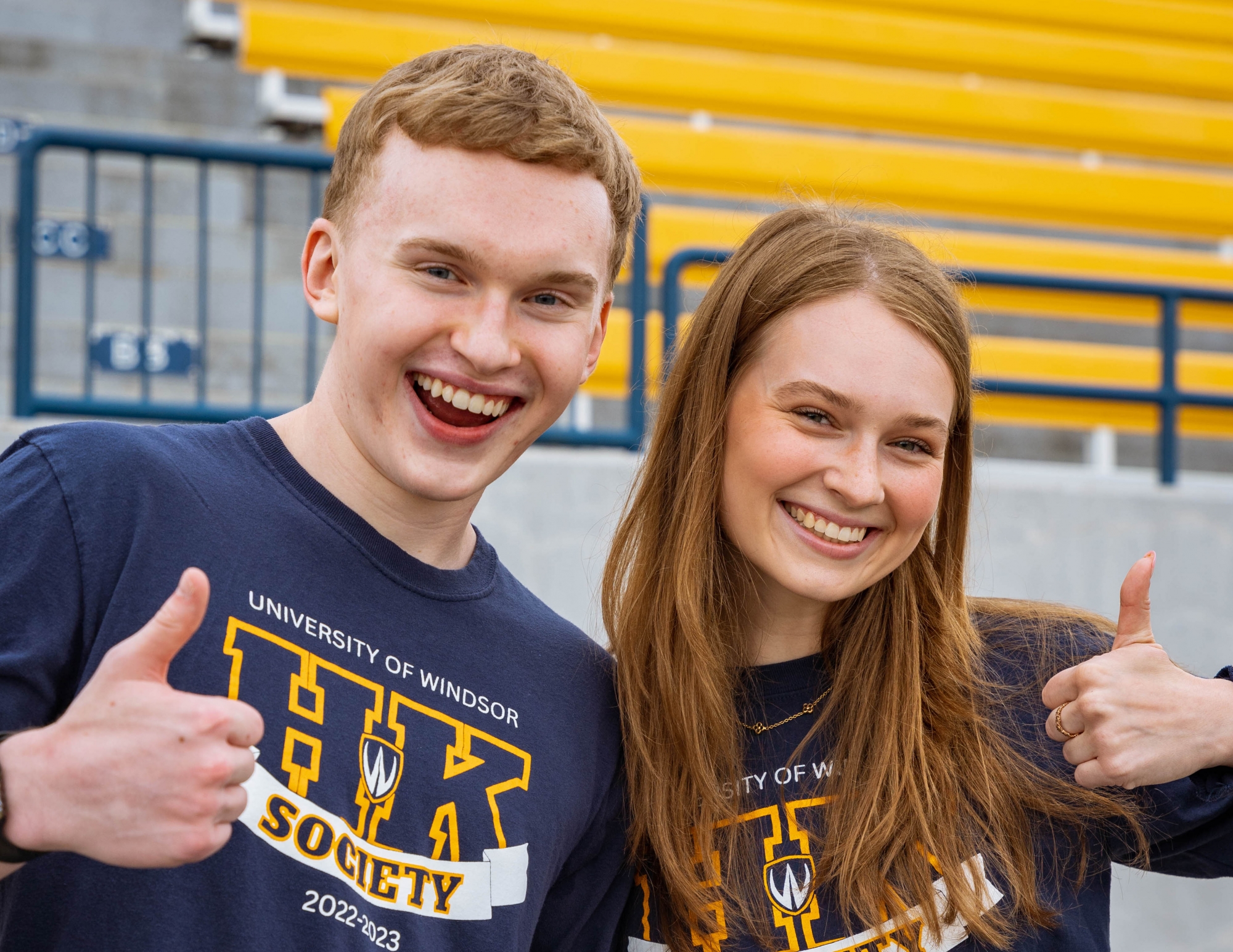 A male and a female student with their thumbs up