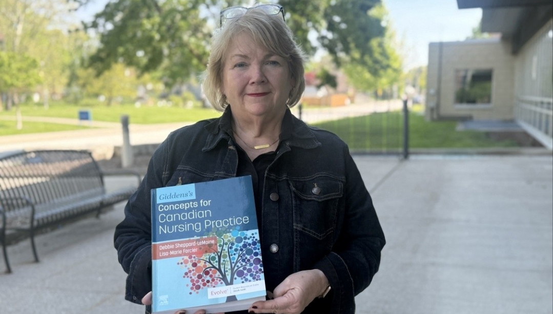 Dean Sheppard-LeMoine stands outside on campus holding the new textbook she co-edited