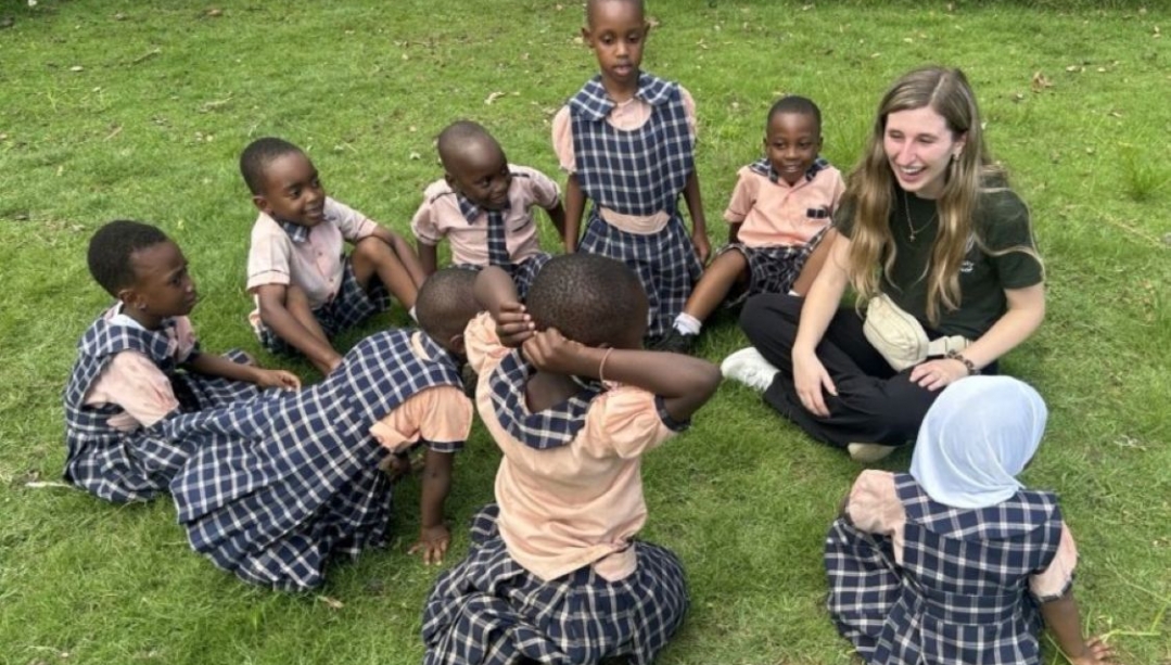 smiling students and a UWindsor teacher candidate sitting in the grass in Tanzania