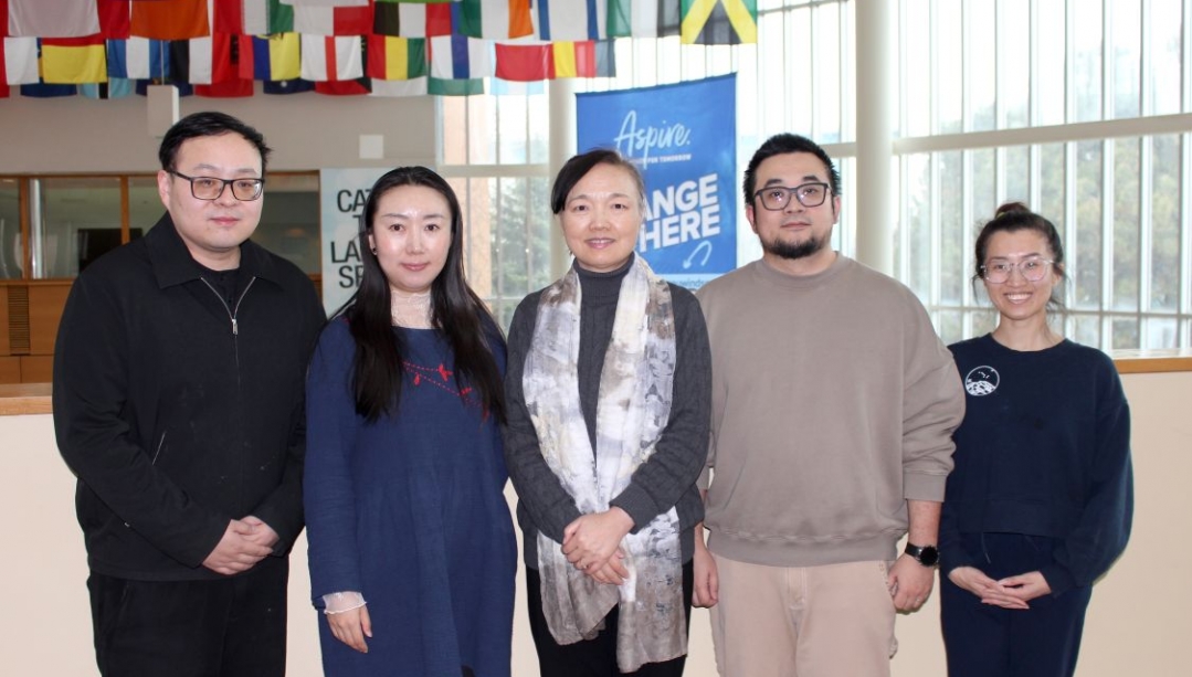 5 people standing in the CAW Student Centre under the flags of many countries with an Aspire banner behind them