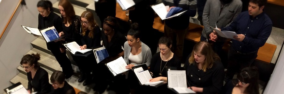 Steveral vertical rows of students, mostly women and all dressed in black or grey, collectively sing in the new Armouries space