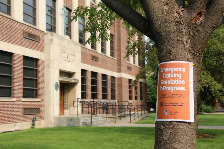 A poster warning of an emergency training scenario is posted on a tree outside Memorial Hall