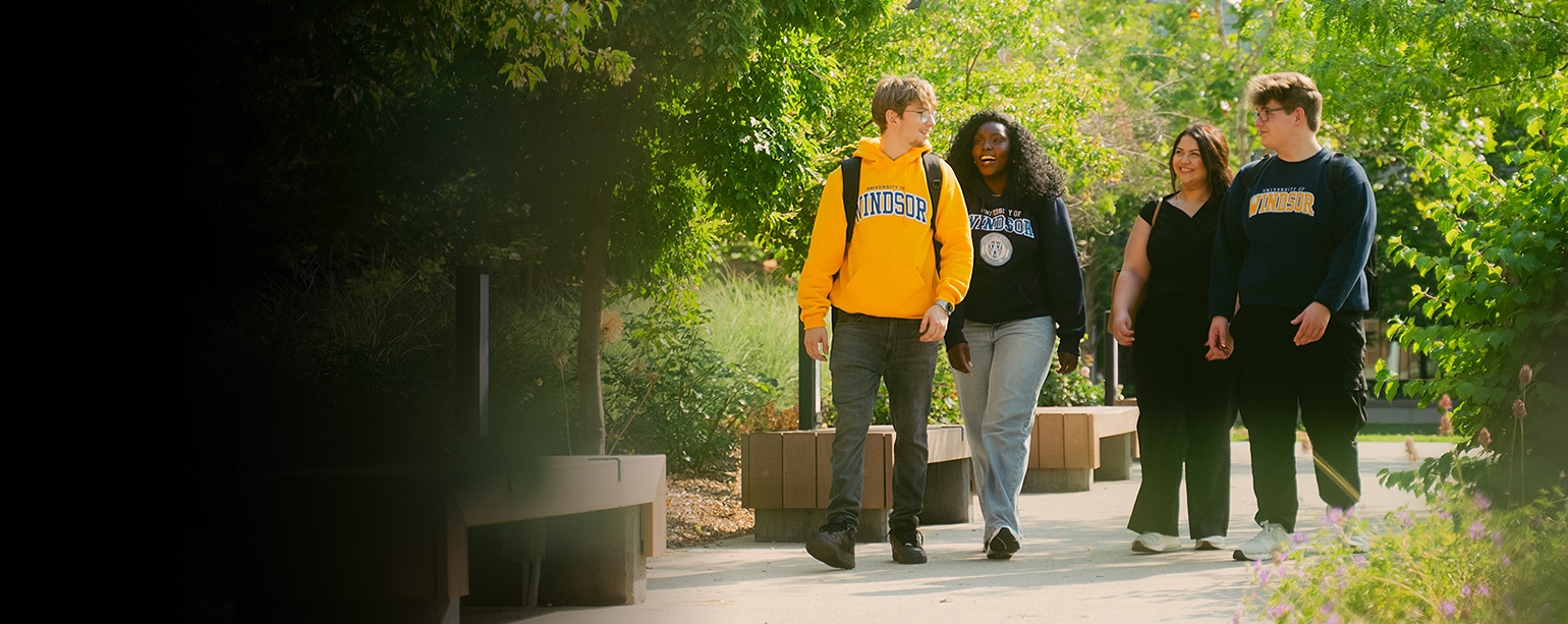 Group of students wearing UWindsor hoodies walking down tree-lined walkway