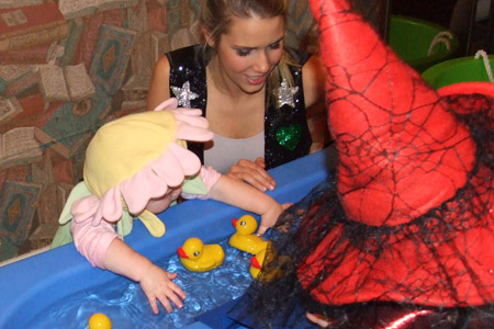 Baby dressed as flower plays with rubber duckies in a pool.