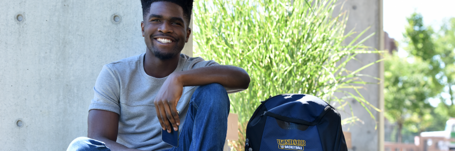 Student sitting on the grass with UWindsor Basketball backpack