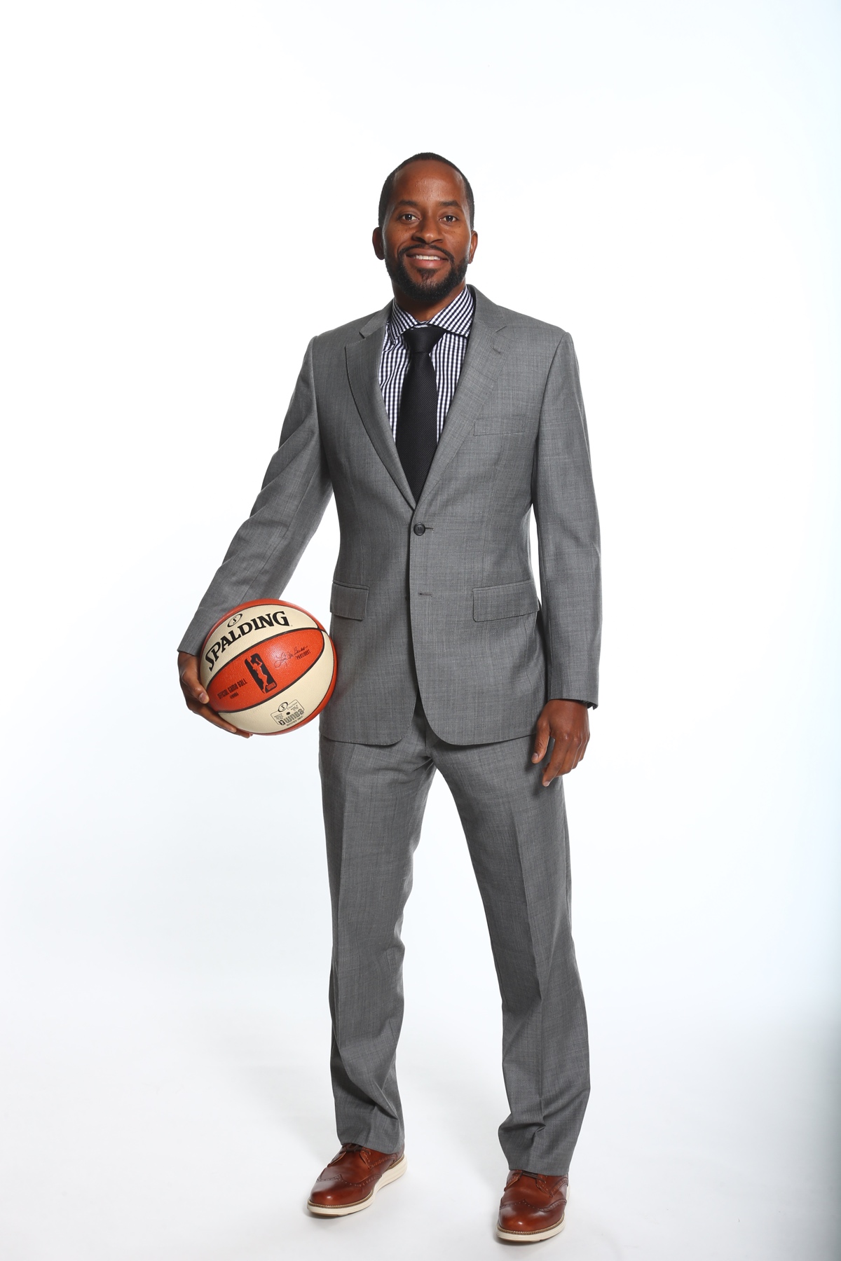 Full-body photo of Sefu Bernard in a grey suit, holding a basketball
