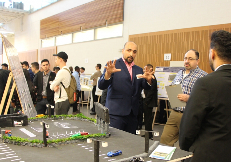 Habib Haider explains his group project, a system designed to reduce the impact of long lines waiting to access the Gordie Howe International Bridge, to professor Hanna Maoh of the Cross-Border Institute.