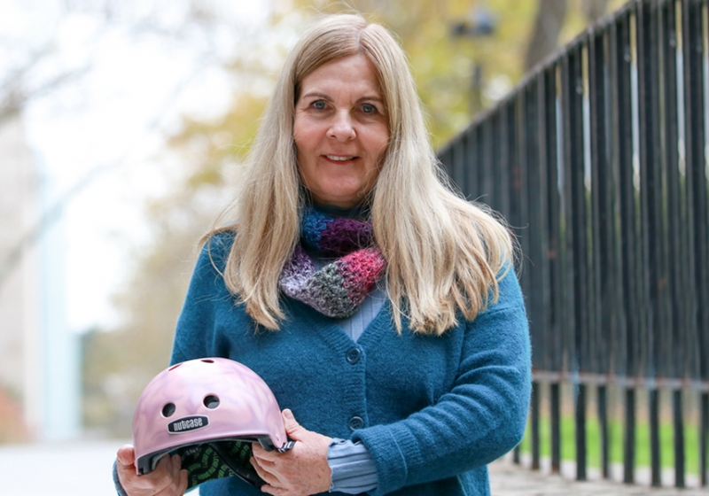Professor Lori Buchanan holds a bicycle helmet, painted as part of the Brain Bucket research project of recent Master’s graduate Daniella Mlinarevic.