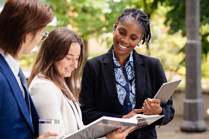 Business students looking at a laptop and book outdoors