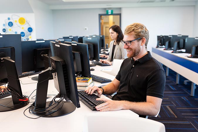 Male MBA student in a computer lab with a female student in background