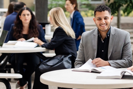 A male and female student sit at a table outside Odette with students seated at another table in background