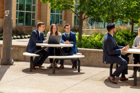 Business students sitting at picnic tables outside of the Odette School of Business building.