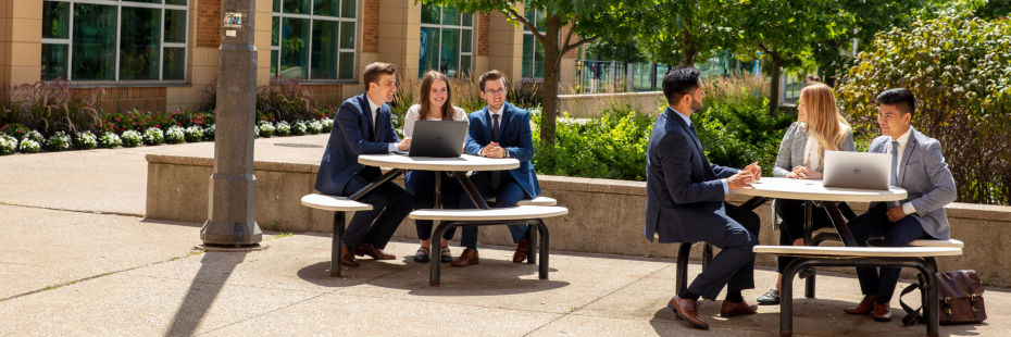 Business students sitting at picnic tables outside of the Odette School of Business building.