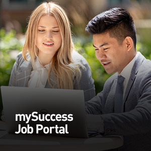 Students in business attire sitting outside and looking at a laptop