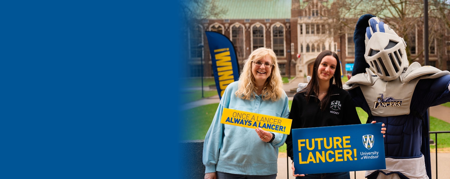 Lancer mascot with two women holding UWindsor Lancer signs. Dillon Hall in background.