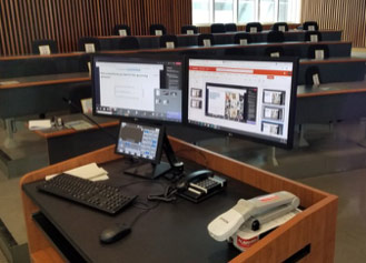 Console set up with dual monitors, crestron panel, phone, and doc camera in classroom