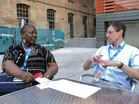 Stephen Bostock and Joy Mighty seated at a table share a conversation.