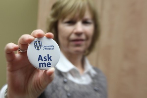 Joanne Gibbs exhibits a button inviting questions from newcomers to campus.