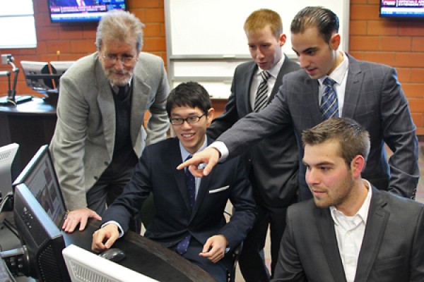 students crowd around a mock trading terminal