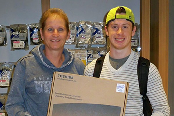 Campus Bookstore employee Lynda Leckie presents a prize laptop to draw winner Daniel Picard.