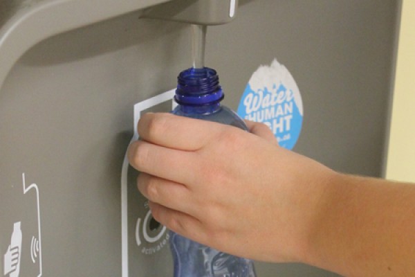hand holds water bottle under refill statiom