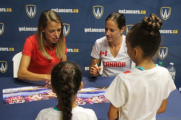 Olympians Melissa Bishop and Noelle Montcalm autograph posters for fans Sienna and Jasmine Benoit.
