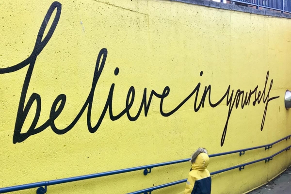 Child standing before billboard &quot;Believe in Yourself&quot;