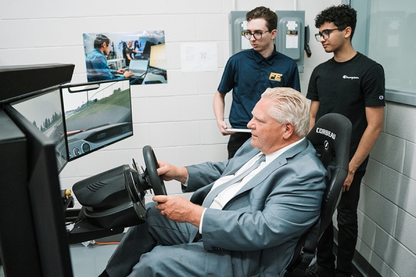 Doug Ford seated at steering wheel before screens simulating road