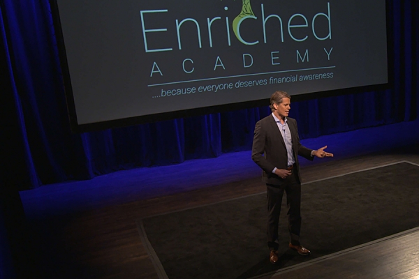 man on stage with banner &quot;Enriched Academy&quot;
