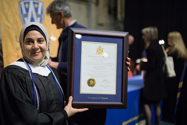 woman in grad robes holding framed diploma