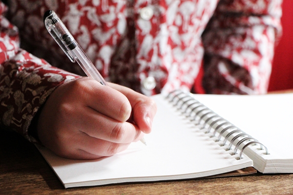 Woman holding pen over creative writing journal.