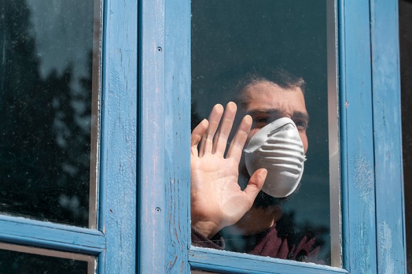 Man wearing face mask looking out window