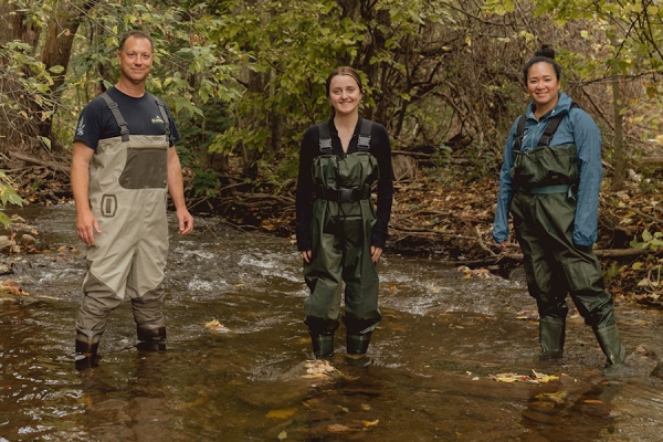 Trevor Pitcher, student Bri Curtis, and Catherine Febria stand in a stream