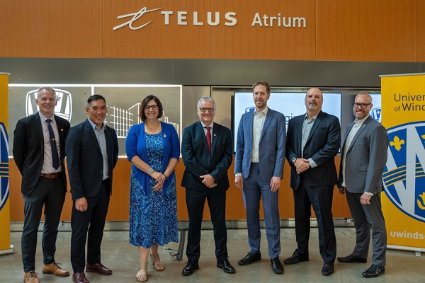Officials from the University and the telecommunications company stand under a sign that reads “Telus Atrium.”