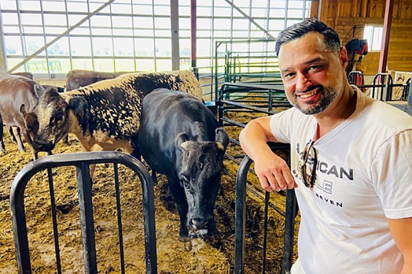 Paolo Vasapolli standing next to cows in pen.