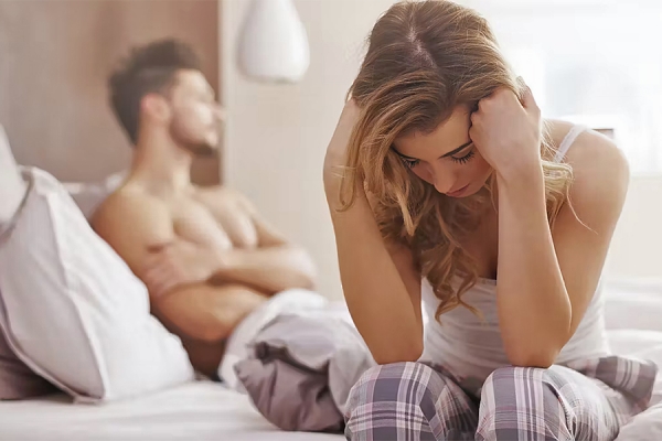 woman sitting on edge of bed looking frustrated, men behind looking away
