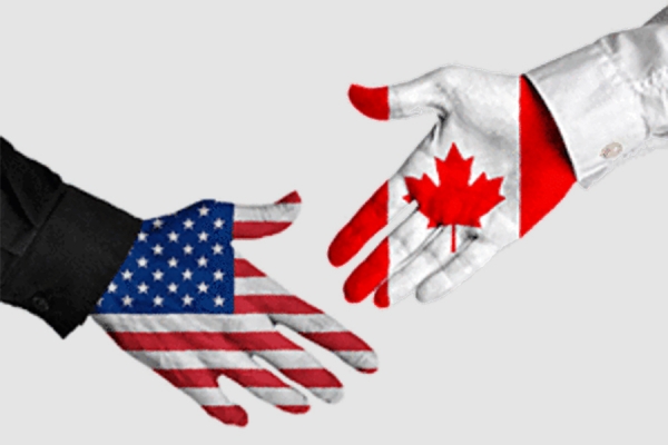 hands reaching to clasp -- one with U.S. flag and one with Canadian flag
